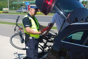 Na zdjęciu umundurowany policjant ruchu drogowego podczas kontroli drogowej sprawdza wyposażenie pojazdu, w ręku trzyma gaśnice.
