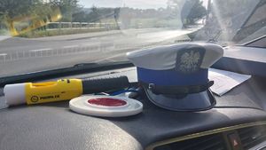 Na zdjeciu, na podszybiu samochodu leży policyjna czapka policjanta ruchu drogowego, urządzenie do kontroli stanu trzeźwości i tarcza do zatrzymywania pojazdów.