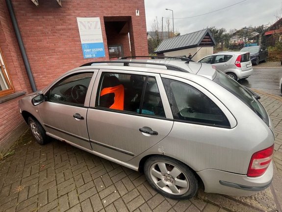 Na zdjeciu pojazd koloru srebrnego przy ścianie narożnej budynku.