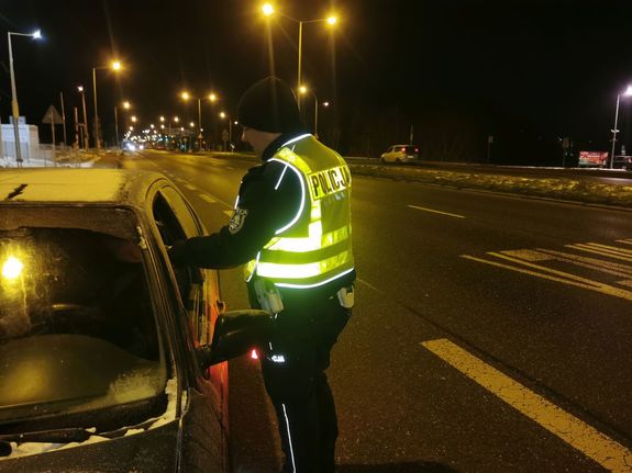 Na zdjęciu umundurowany policjant w żółtej odblaskowej kamizelce podczas kontroli stanu trzeźwości kierującego.