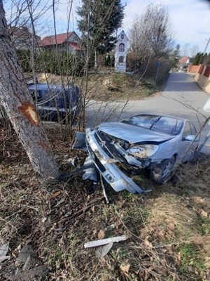 Na zdjęciu rozbity pojazd citroen c5 z uszkodzonym przodem , z jego lewej strony drzewo z uszkodzoną korą. W tle kapliczka i domy.