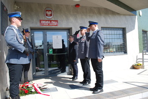 Na zdjęciu po lewej stronie warta honorowa policjantów przy tablicy z nazwiskami zamordowanych przez NKWD policjantów, która zawieszona jest na ścianie komisariatu w Głogowie Małopolskim. Na wprost tablicy stoją od lewej aspirant sztabowy Paweł Maj, Komendant Miejski Policji w Rzeszowie insp. Bogusław. Kania. Policjanci ubrani są w mundury galowe i oddają honory. Obok Komendanta Miejskiego stoi Burmistrz Głogowa Małopolskiego Paweł Baj.