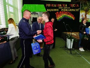 Na zdjęciu Zastępca Komendanta Miejskiego Policji w Rzeszowie mł. insp. Marek Worek wręczający nagrodę laureatowi  konkursu. W tle inny zaproszeni goście.