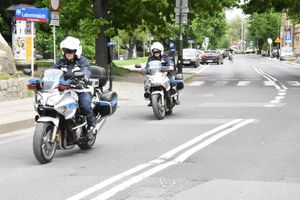 Na zdjęciu policjanci w pełnym umundurowaniu jadący na motorach służbowych. W tle drzewa.