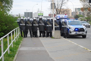 Na zdjęciu pluton umundurowanych policjantów. Obok radiowozy.