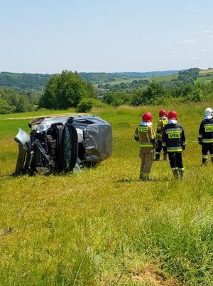 Na  leżący na boku pojazd suzuki z widocznymi uszkodzeniami, bok  niego strażacy biorący udział w akcji.