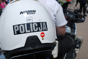 Na zdjęciu policyjny motocykl, na którym tyłem siedzi policjant ubrany w biała koszulkę z napisem policja na plecach.