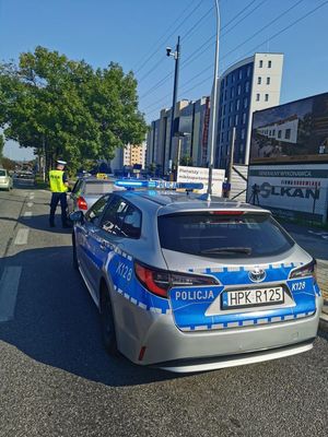 Na zdjeciu umundurowany policjant kontroluje pojazd, za którym stoi radiowóz.