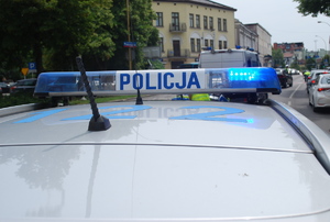 Na zdjeciu belka policyjnego radiowozu z napisem policja. W tle budynki.