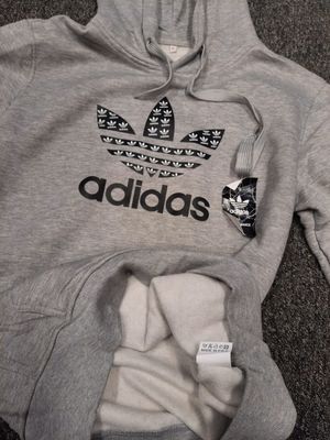 Na zdjęciu bluza z kapturem koloru szarego, z przodu logo i napis adidas.