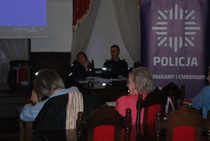 Na zdjęciu sala sesyjna rzeszowskiego Ratusza i zgromadzeni w niej goście. W tle na środku przy stole siedzą policjanci w niebieskich mundurach, biorący udział w debacie. Od lewej: mł. asp. Ewa Saidło, asp. sztab. Jerzy Suszyński. Z prawej strony wisi baner z logiem policji i napisem policja pomagamy i chronimy.