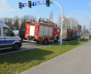 Na zdjęciu policyjny radiowóz, przed nim wóz strażacki, przed nim autobus i auto osobowe. Po bokach stoją strażacy i przechodnie.