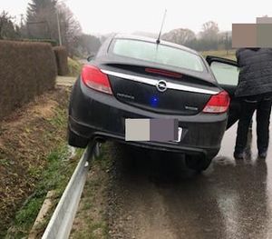 Na zdjęciu pojazd marki opel, lewą stroną najechał na barierę drogową. Obok z prawej strony stoi ubrany na ciemno mężczyzna.