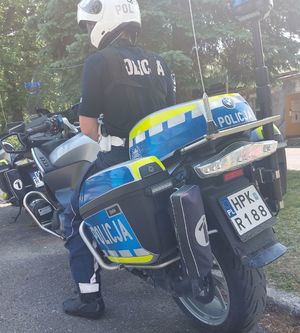 Na zdjęciu tyłem policyjny motocykl na którym siedzi umundurowany policjant. Na głowie ma biały kask.