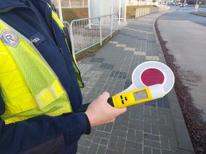 Na zdjęciu policjant w umundurowaniu trzyma w ręce tarczę do zatrzymywania pojazdów i urządzenie do kontroli stanu trzeźwości.