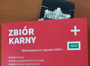 Na zdjęciu zbiór przepisów kodeks karny i inne, między kartkami włożona jest policyjna odznaka.