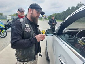 Na zdjęciu motocyklista z klubu motocyklowego trzyma w dłoni naklejkę zmieścimy się wszyscy podczas rozmowy z kierującym pojazdem, zatrzymanym do kontroli drogowej.