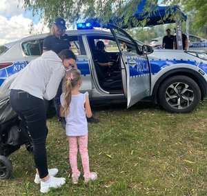 Na zdjęciu policyjny radiowóz przed którym stoi dziewczynka i kobieta.