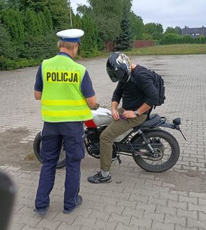 Na zdjeciu umundurowana policjantka ruchu drogowego podczas kontroli drogowej motocyklisty.