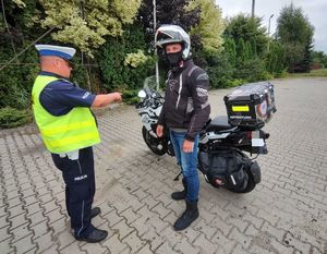 Na zdjeciu umundurowany policjant ruchu drogowego podczas kontroli drogowej motocyklisty.