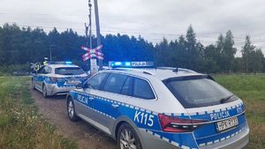 Na zdjęciu dwa policyjne radiowozy przed przejazdem kolejowym, w tle umundurowani policjanci.