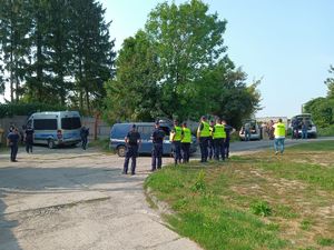 Na zdjęciu umundurowaniu policjanci oraz w ubraniach cywilnych w żółtych kamizelkach, dalej policyjne radiowozy.