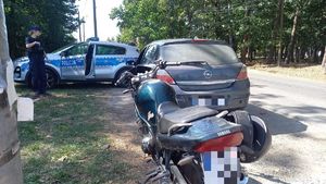 Na zdjęciu motocykl marki Yamaha, przed num samochód marki Opel. Dalej z lewej strony umundurowana policjantka i policyjny radiowóz.