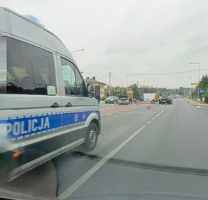 Na zdjeciu policyjny ambulans ruchu drogowego, w tle pojazdy biorące udział w zdarzeniu.