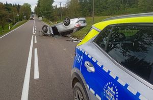 Na zdjęciu policyjny radiowóz i przewrócony na dach samochód osobowy.