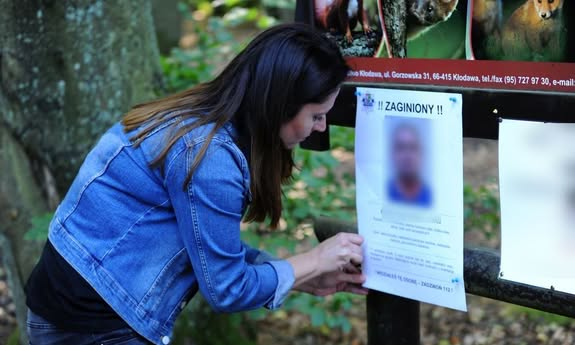 Na zdjęciu kobieta z długimi włosami, ubrana w jeansową kurtkę przypina na tablicy ogłoszeń plakat.