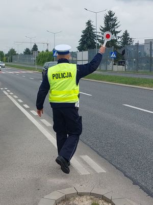 Na zdjęciu umundurowany policjant ruchu drogowego. W prawe podniesionej ręce trzyma tarczę do zatrzymywania pojazdów.