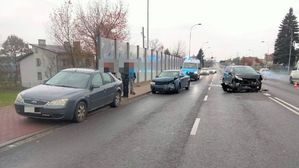 Na jezdni trzy pojazdy jakie brały udział w zdarzeniu drogowym, za nimi policyjny ambulans ruchu drogowego, w tle inne przejeżdżające pojazdy.