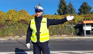 Na zdjeciu umundurowany policjant ruchu drogowego ręcznie kieruje ruchem na skrzyżowaniu.