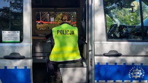 Na zdjęciu policjant w żółtej kamizelce odblaskowej z napisem policja na plecach, siedzi w policyjnym busie,