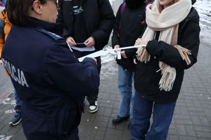 Na zdjęciu umundurowana policjanta rozdaje pieszym odblaskowe opaski.