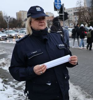 Na zdjęciu umundurowana policjantka trzyma w rękach odblaskowe opaski.