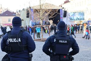 Na zdjęciu tyłem dwoje umundurowanych policjantów, w tle scena,