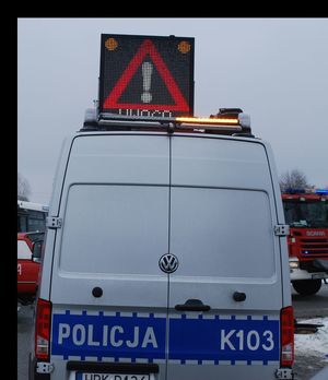 Na zdjęciu policyjny ambulans ruchu drogowego. Na dachu wysunięta tablica świetlna informująca o wypadku drogowym.