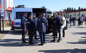 Na zdjęciu policyjny ambulans ruchu drogowego, obok stoją umundurowani policjanci oraz młodzież szkolna.