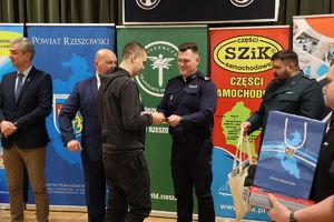 Na zdjęciu w środkowej części p.o. Zastępca Komendanta Miejskiego Policji w Rzeszowie podinsp. Maciej Gawryś wręcza nagrodę chłopcu - jednemu z laureatów konkursu. Z prawej i lewej strony komendanta inni zaproszeni goście.