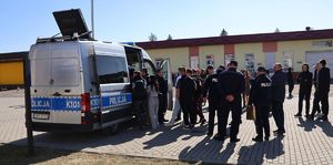 Na zdjęciu policyjny ambulans ruchu drogowego, obok stoją umundurowani policjanci oraz młodzież szkolna.