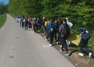 Na zdjęciu idąca poboczem młodzież z workami do segregacji odpadów, na czele policyjny radiowóz.