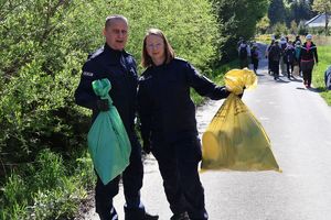 Na zdjeciu dwoje umundurowanych policjantów niosących worki ze śmieciami. Przed nimi dzieci.