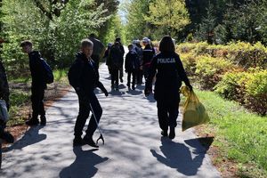 Na zdjeciu idąca tyłem umundurowana policjantka, w prawej ręce trzyma worek ze śmieciami, obok niej uczniowie.