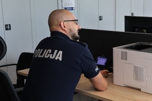 Na zdjęciu umundurowany policjant siedzi przy biurku.