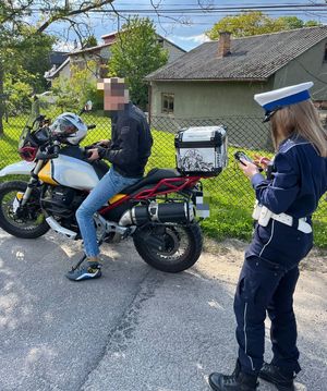 Na zdjęciu policjantka ruchu drogowego w trakcie kontroli drogowej motocyklisty,który siedzi na motorze.