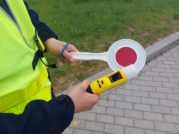 Na zdjeciu umundurowany policjant trzyma w ręku urządzenie do kontroli stanu trzeźwości i tarczę do zatrzymywania pojazdów.
