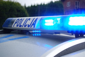 Na zdjęciu beka policyjnego radiowozu z napisem policja z włączonymi światłami barwy niebieskiej.