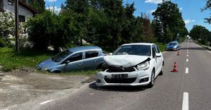 Zdjęcie z miejsca wypadku w Łubnie. Uszkodzony pojazd citroen koloru białego i pojazd opel corsa koloru niebieskiego. W tle policyjny radiowóz