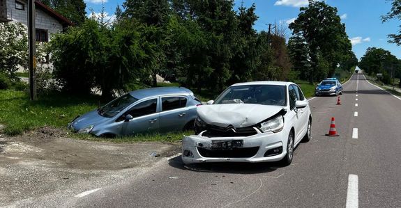 Zdjęcie z miejsca wypadku w Łubnie. Uszkodzony pojazd citroen koloru białego i pojazd opel corsa koloru niebieskiego. W tle policyjny radiowóz